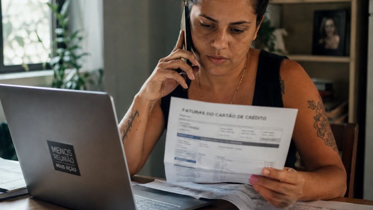 Mulher ao telefone negociando taxa de juros do cartão de crédito com fatura na mesa