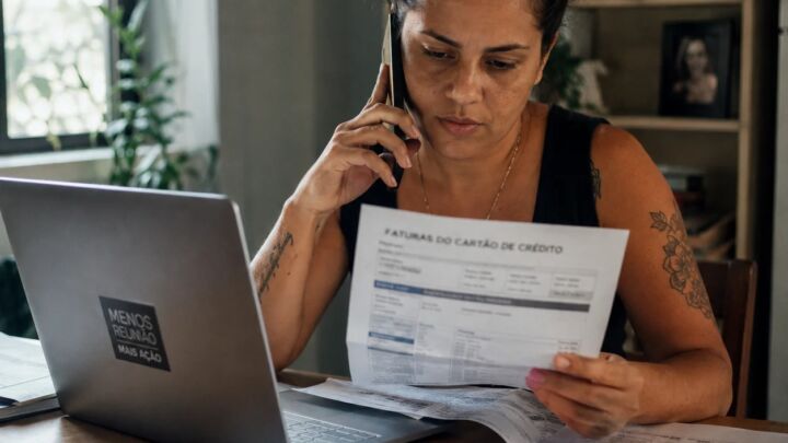 Mulher ao telefone negociando taxa de juros do cartão de crédito com fatura na mesa
